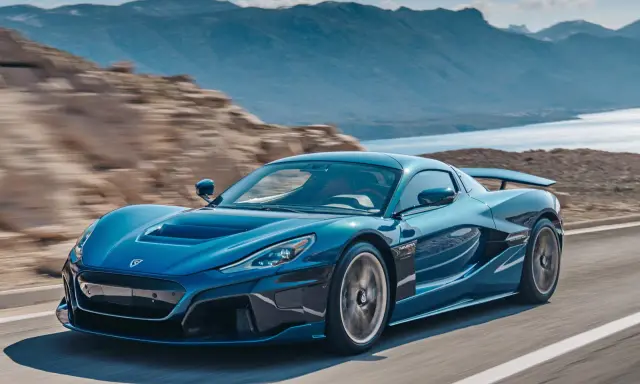 La Rimac Nevera blu sfreccia su una strada panoramica, con montagne e acqua sullo sfondo.