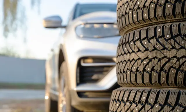 Gomme chiodate in primo piano, con un'auto bianca sfocata sullo sfondo. Mi chiedo se posso montare gomme con altezza diversa per affrontare ogni tipo di terreno.