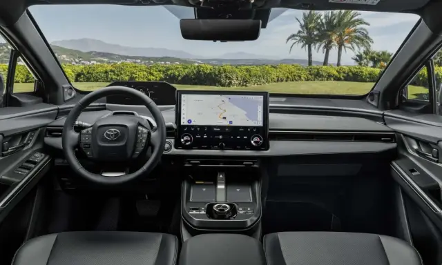 Interni moderni della Toyota bz4x con ampio display centrale e volante multifunzione. Navigazione attiva per un viaggio panoramico.