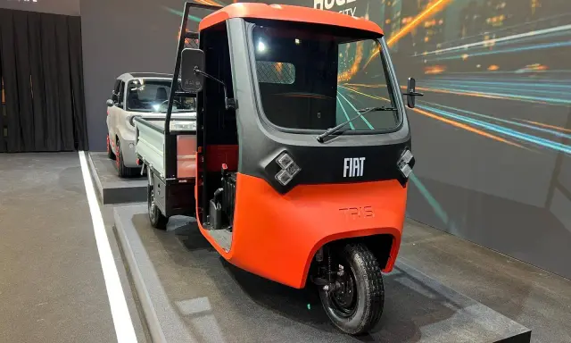 Un vivace Fiat Tris arancione e grigio, un veicolo a tre ruote per il trasporto merci, esposto su una pedana.