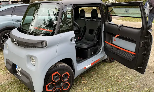 Un'auto elettrica due posti grigia con dettagli arancioni, porte aperte, sedili neri e cerchi distintivi.