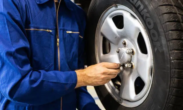 Meccanico in tuta blu controlla i bulloni di una ruota. Ci si chiede dopo quanti km si cambiano le gomme per sicurezza.