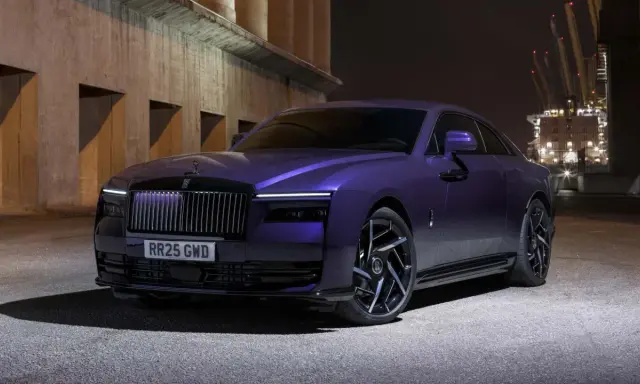Una Rolls-Royce sportiva viola metallizzato, con un design audace e cerchi neri, parcheggiata di notte vicino a un porto industriale.