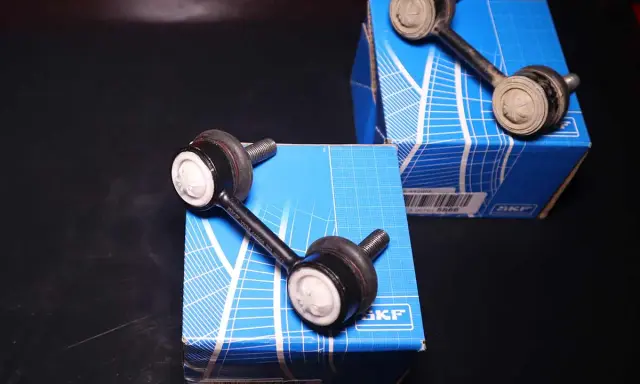 Due biellette auto SKF, componenti essenziali per la stabilità del veicolo, posizionate su scatole blu.