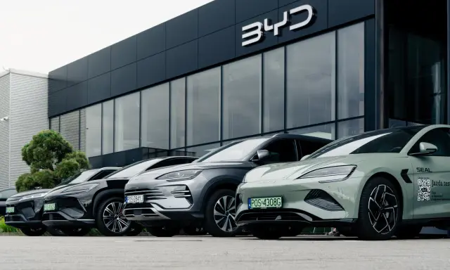 Vari modelli di auto BYD parcheggiati davanti a uno showroom moderno.