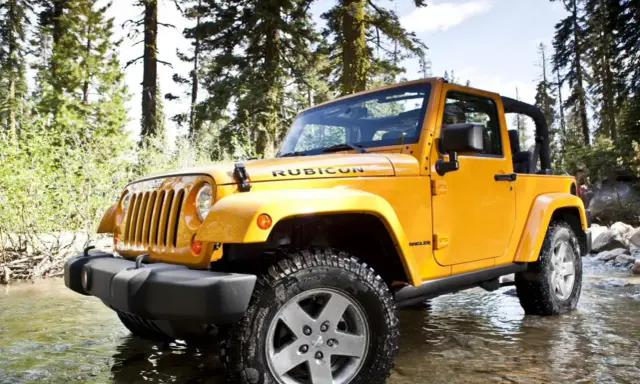 Jeep Wrangler 2.8 CRD in giallo, immerso in un ruscello tra alberi. Un'avventura che potrebbe presentare qualche problema.
