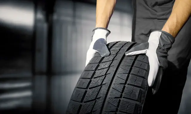 Mani guantate tengono un nuovo pneumatico. Quanto tempo ci vuole per cambiare 4 gomme? Dipende dall'officina!