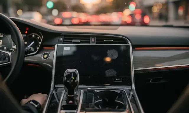 Interno di un'auto moderna, con cambio automatico e schermo touch. La mano del guidatore è sul cambio, pronto per un viaggio in **auto hold golf**.