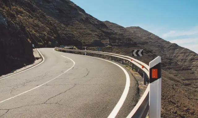 Strada tortuosa in montagna con guardrail e segnali di pericolo. I catadiottri cosa sono? Sono quei dispositivi che riflettono la luce per segnalare la strada.