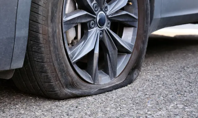 Gomma bucata dell'auto, sgonfia e appoggiata sull'asfalto. Un inconveniente che ferma ogni viaggio.
