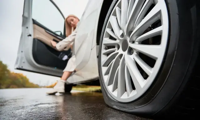 Donna esce dall'auto con gomme sgonfie sul bagnato.