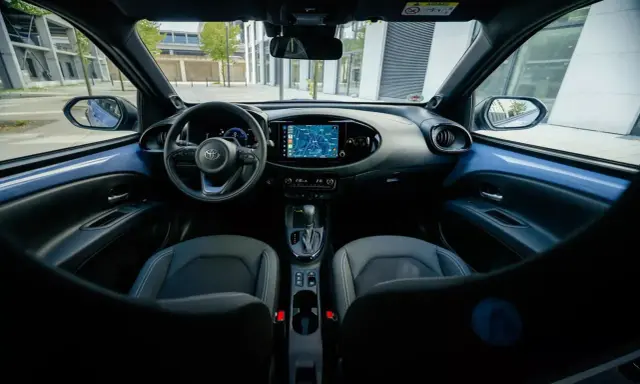 Interni moderni della Toyota Aygo X: volante, cruscotto con navigatore e sedili in tessuto.