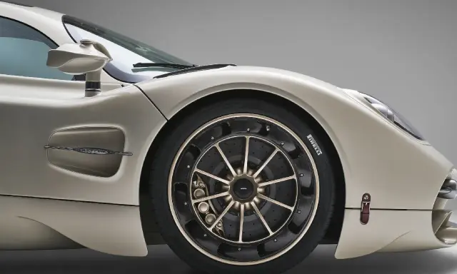 Dettaglio di un'auto sportiva color champagne, con focus sul montaggio pneumatici e cerchi in lega dorati.