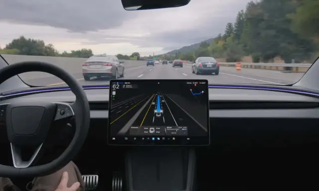 Interno di una Tesla con il sistema FSD attivo, mostra la guida autonoma in autostrada con visualizzazione delle auto circostanti.