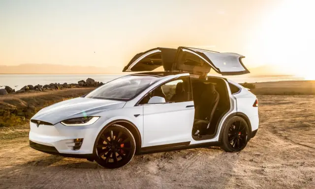 Tesla Model X bianca con portiere ad ali di gabbiano aperte al tramonto, un'auto elettrica che rappresenta il lusso e l'innovazione, forse la tesla più costosa.