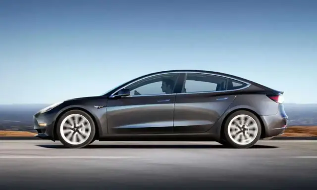 Tesla grigia in movimento su strada, con un conducente al volante. Quanti km fa una Tesla? Dipende dal modello e dalla batteria.