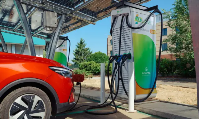 Un'auto rossa si ricarica presso colonnine ultra fast sotto pannelli solari.