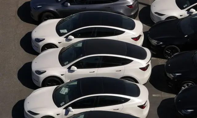 Parcheggio di auto elettriche in Italia, con modelli bianchi e grigi in fila, pronti per la consegna.