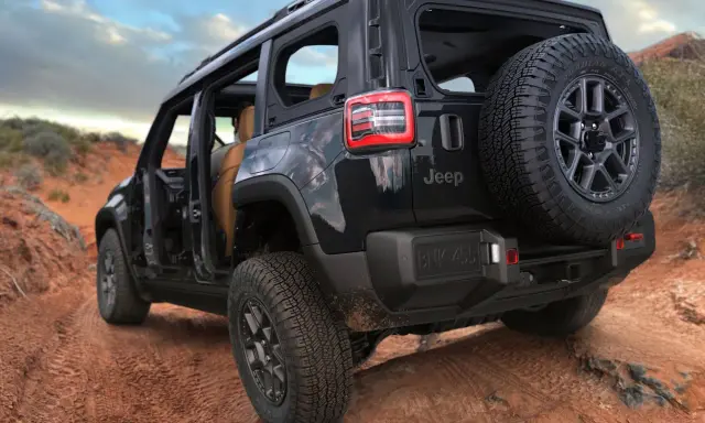 Un fuoristrada elettrico Jeep nero affronta un sentiero sterrato nel deserto, con le portiere aperte e una ruota di scorta sul retro.