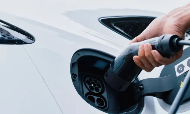 Mano inserisce la spina per trasformare l'auto in elettrica. Ricarica di un veicolo a zero emissioni.