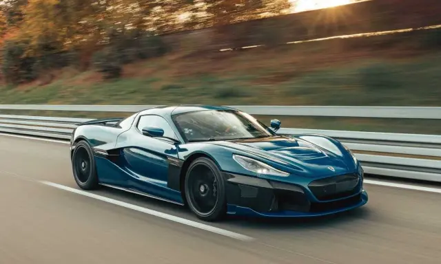 La **auto elettrica più veloce** sfreccia su una strada, con il sole che tramonta tra gli alberi sullo sfondo.