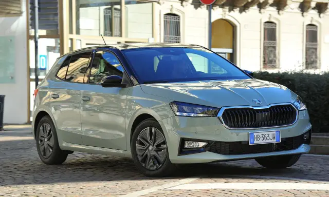 A light green Skoda Fabia hatchback with a black roof is parked on a cobblestone street in front of a building.