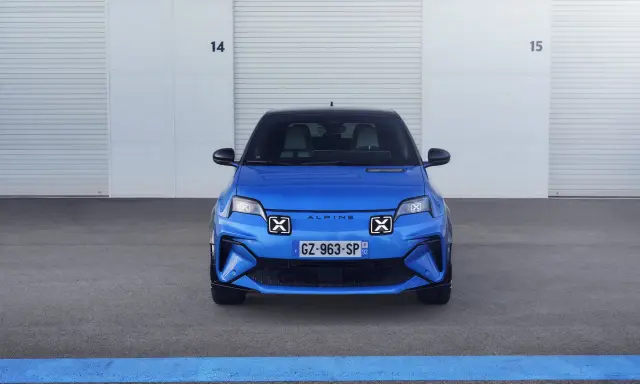 La nuova Alpine A290, un'auto elettrica sportiva blu brillante, attende il suo momento davanti a un garage con porte chiuse.