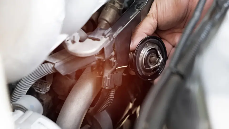 Mano che rimuove il termostato macchina, componente essenziale per il controllo della temperatura del motore.