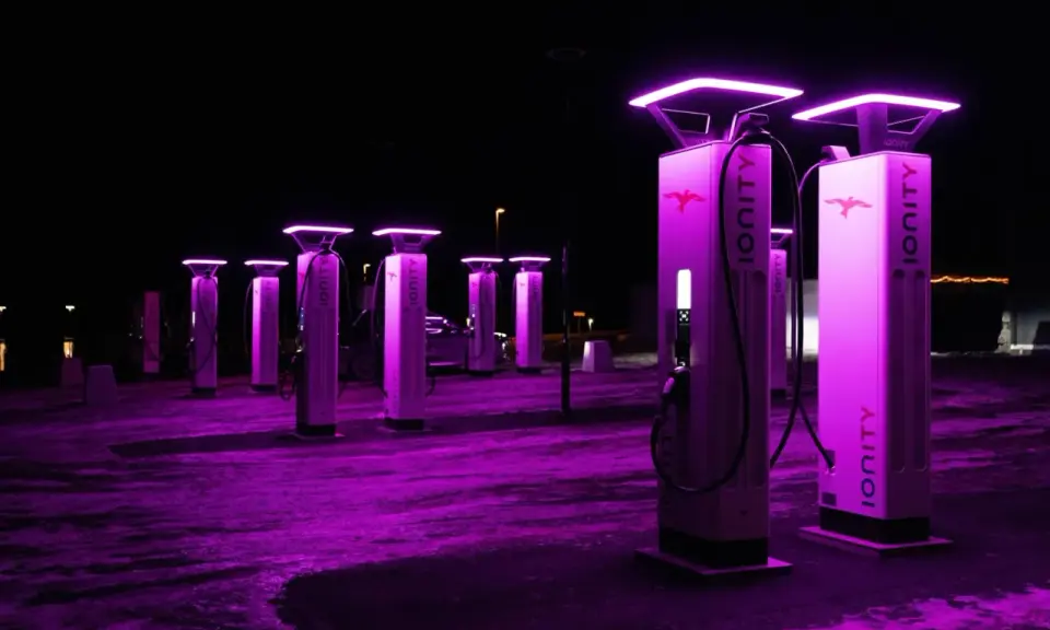 Stazione di ricarica Ionity Italia di notte, illuminata da luci viola. Colonne moderne con logo e cavi pronti per le auto elettriche.