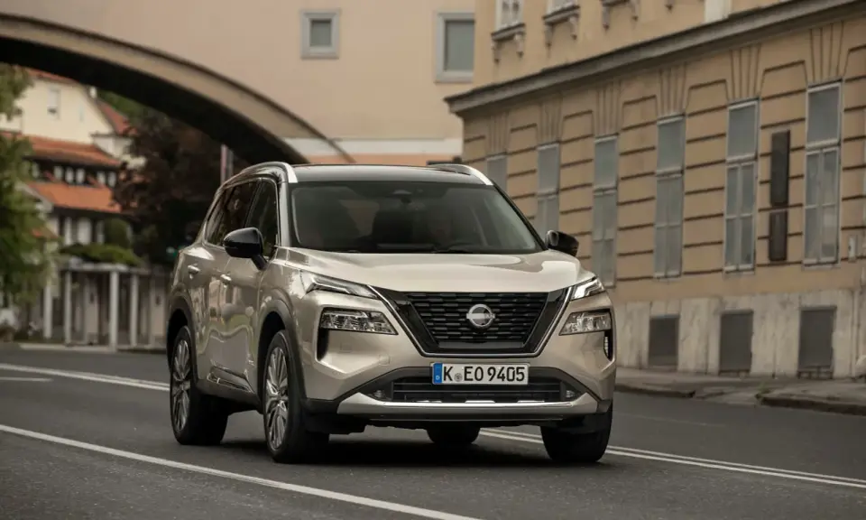 Nissan X-Trail full hybrid beige, in corsa su strada urbana con edifici storici sullo sfondo.