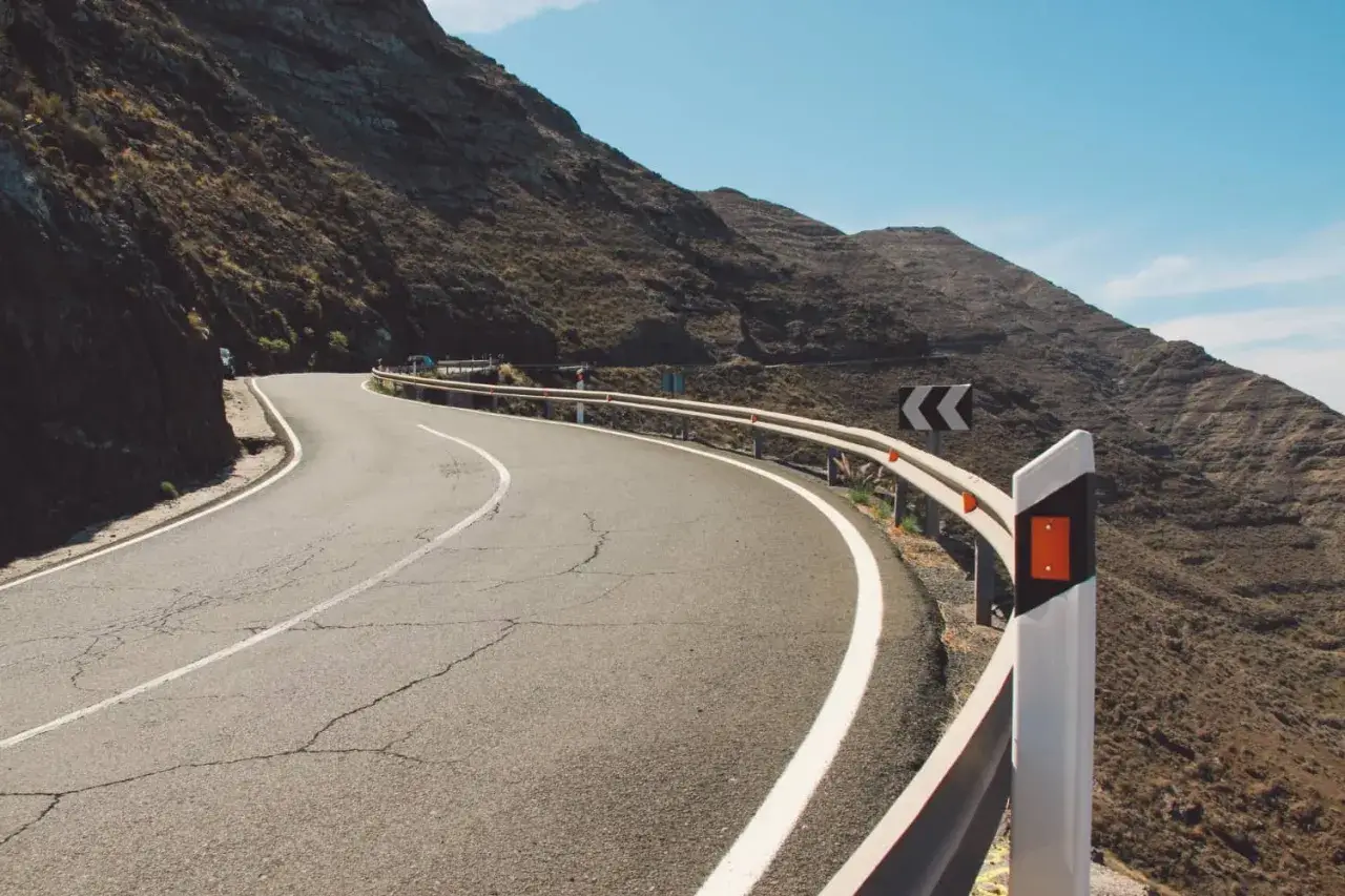 Strada tortuosa in montagna con guardrail e segnali di pericolo. I catadiottri cosa sono? Sono quei dispositivi che riflettono la luce per segnalare la strada.