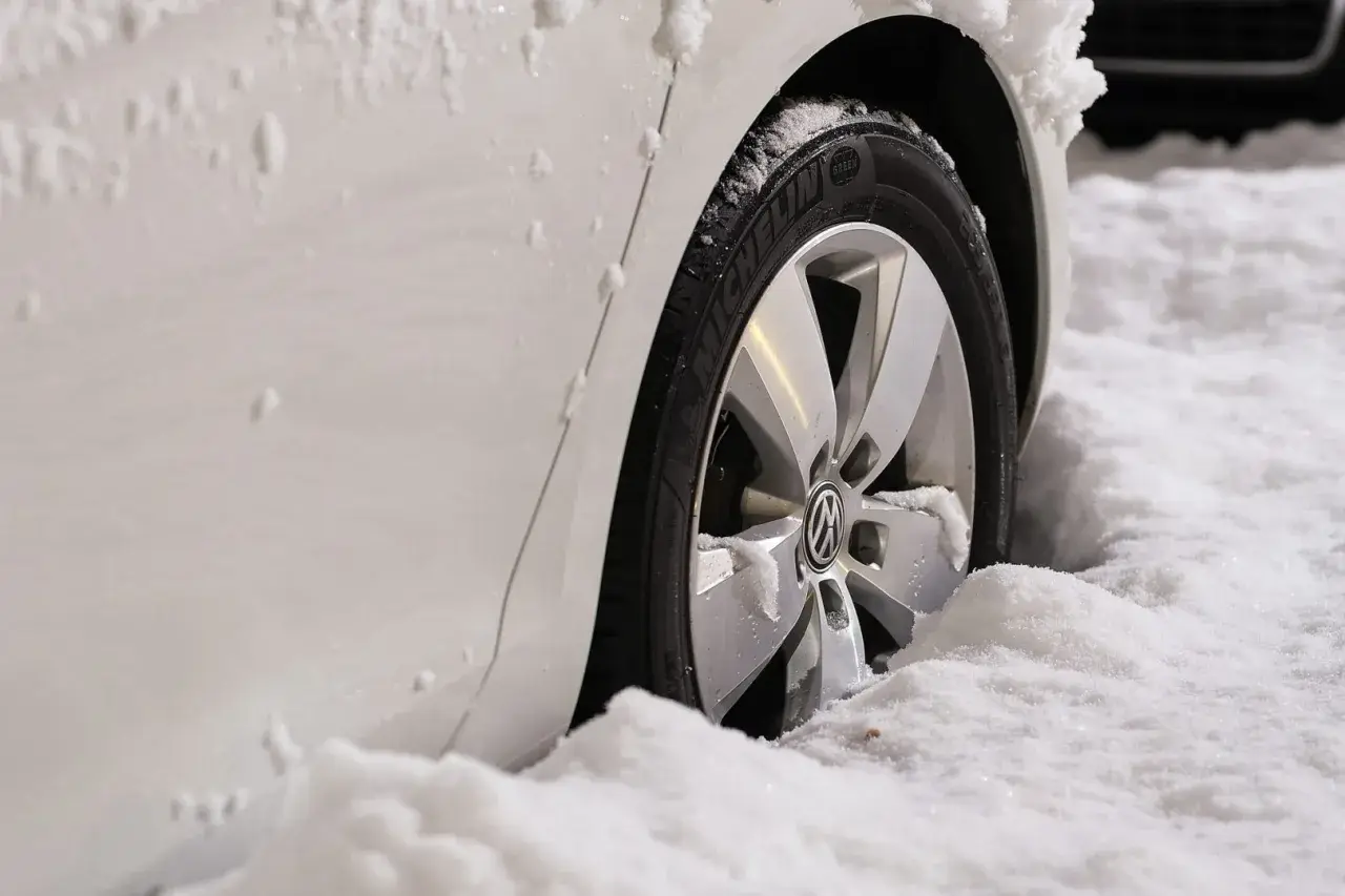 Ruota di un'auto bianca sommersa dalla neve. Il freno a mano ghiacciato rende difficile muoversi.