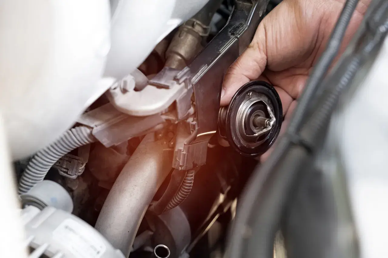 Mano che rimuove il termostato macchina, componente essenziale per il controllo della temperatura del motore.