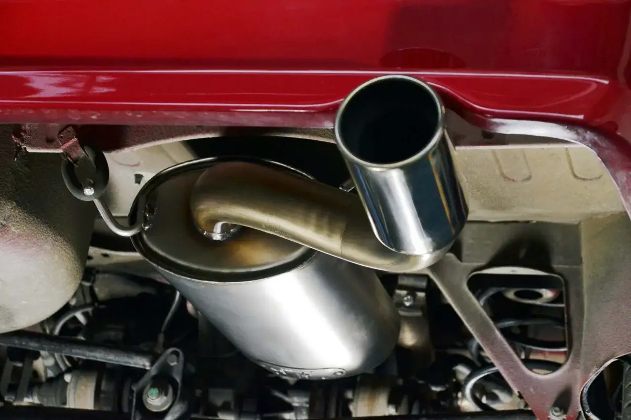 Il tubo di scappamento auto cromato brilla sotto la carrozzeria rossa, pronto a liberare i gas di scarico.