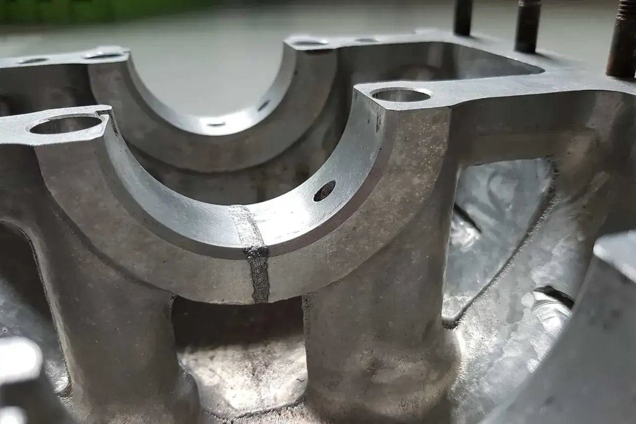 Parti metalliche di un motore con saldatura visibile su un supporto, suggerendo un albero motore rotto.