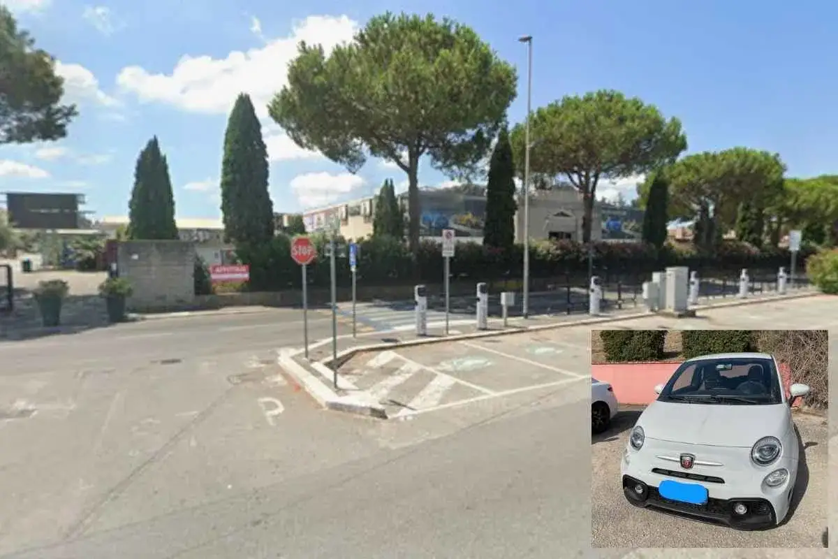 Un'auto bianca, tra le auto più rubate in Italia, parcheggiata vicino a colonnine di ricarica elettrica in una giornata di sole.