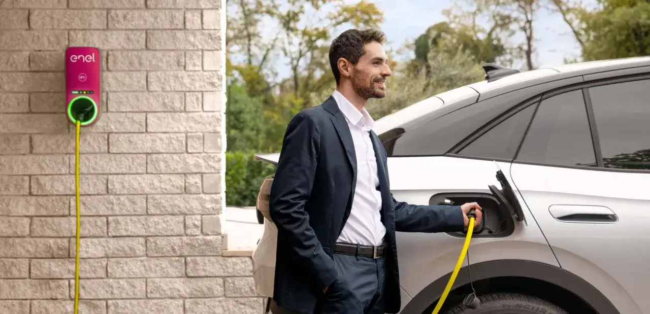 Uomo in giacca collega auto elettrica a wallbox Enel. Scopri il costo installazione wallbox Enel per una ricarica comoda.