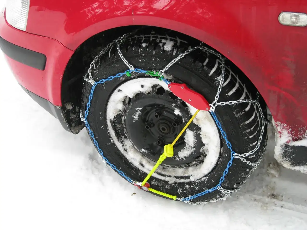 Ruota di un'auto rossa con catene da neve montate su pneumatici invernali, pronte per affrontare la neve.