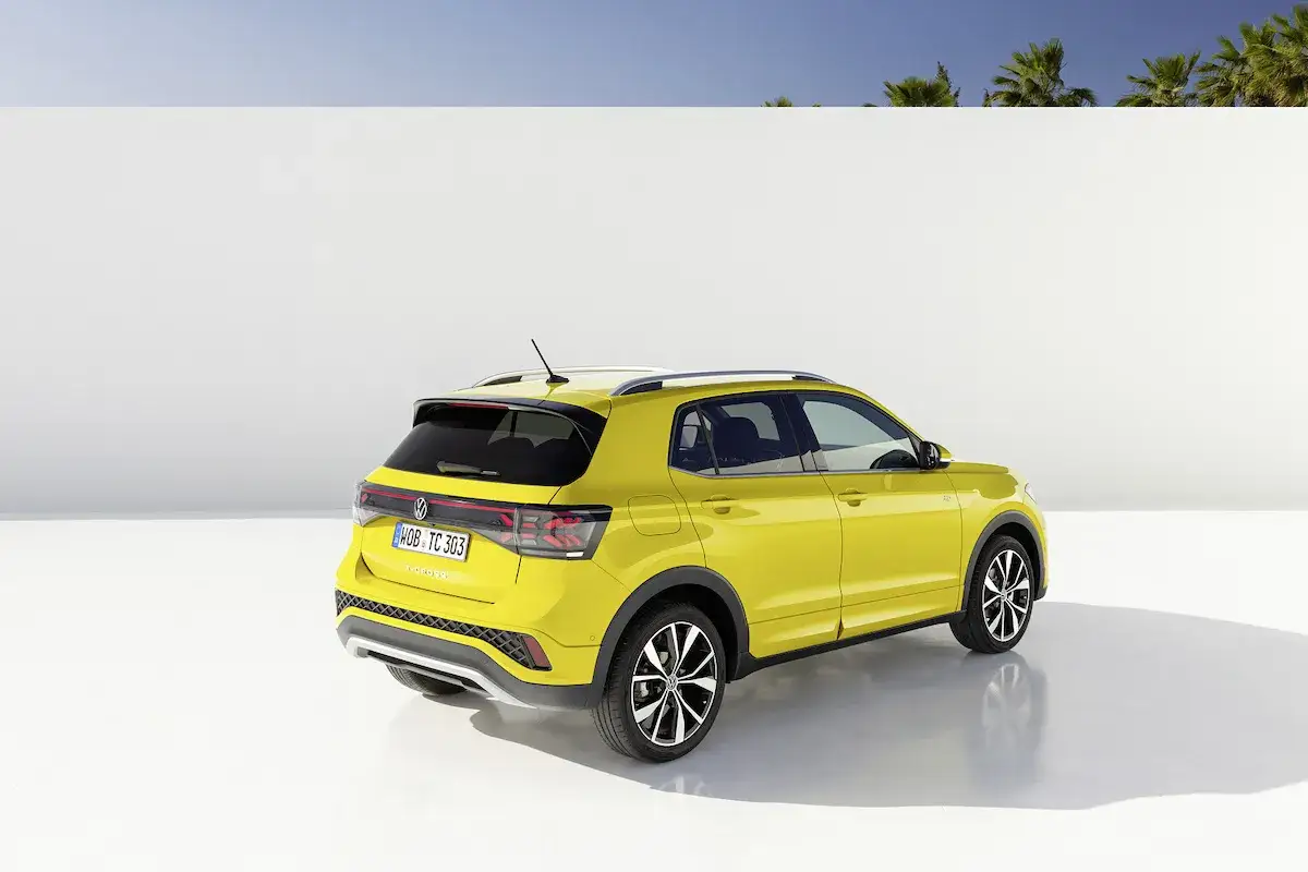 Un vivace Volkswagen T-Cross giallo brillante, pronto per ogni avventura, si staglia contro uno sfondo bianco e un cielo azzurro.