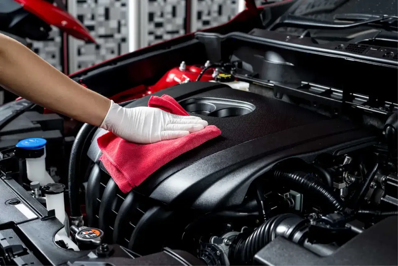 Mano con guanto bianco pulisce motore auto con panno rosso. La decarbonizzazione motore pro e contro è un tema importante per la manutenzione.