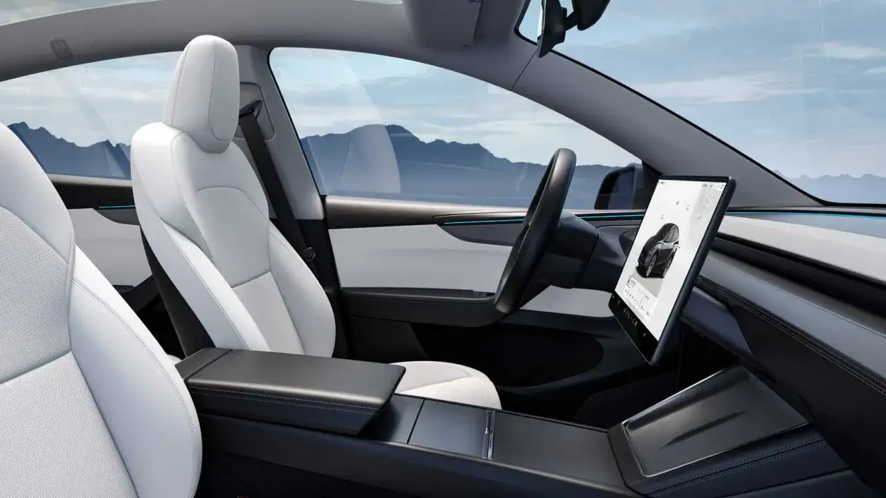 Interni minimalisti e luminosi del tesla model y, con sedili bianchi in pelle e un grande schermo centrale.