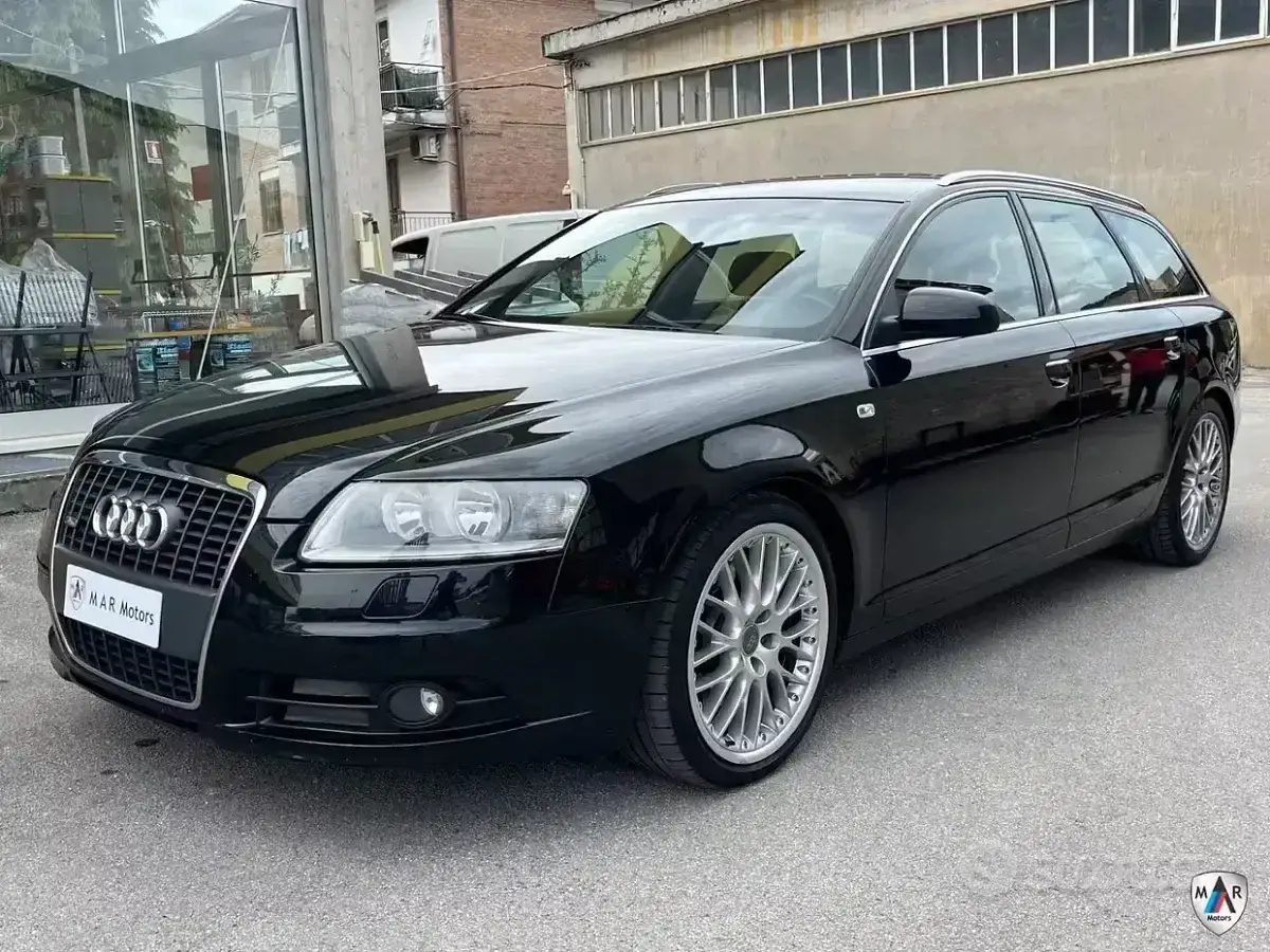Audi A6 C6 Avant nera lucida, con cerchi in lega argentati, parcheggiata all'esterno di un edificio.