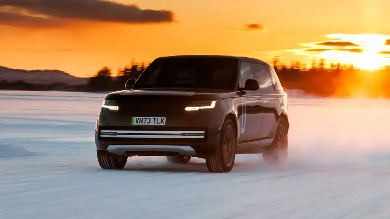 La nuova range rover elettrica sfreccia su una distesa innevata al tramonto, sollevando una nuvola di polvere.