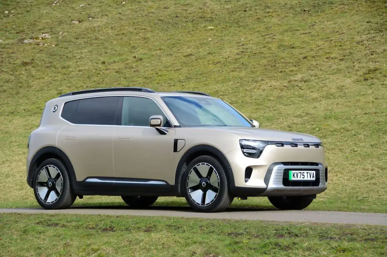 La nuova smart, un SUV elettrico color champagne, si muove su una strada sterrata con un prato verde sullo sfondo.