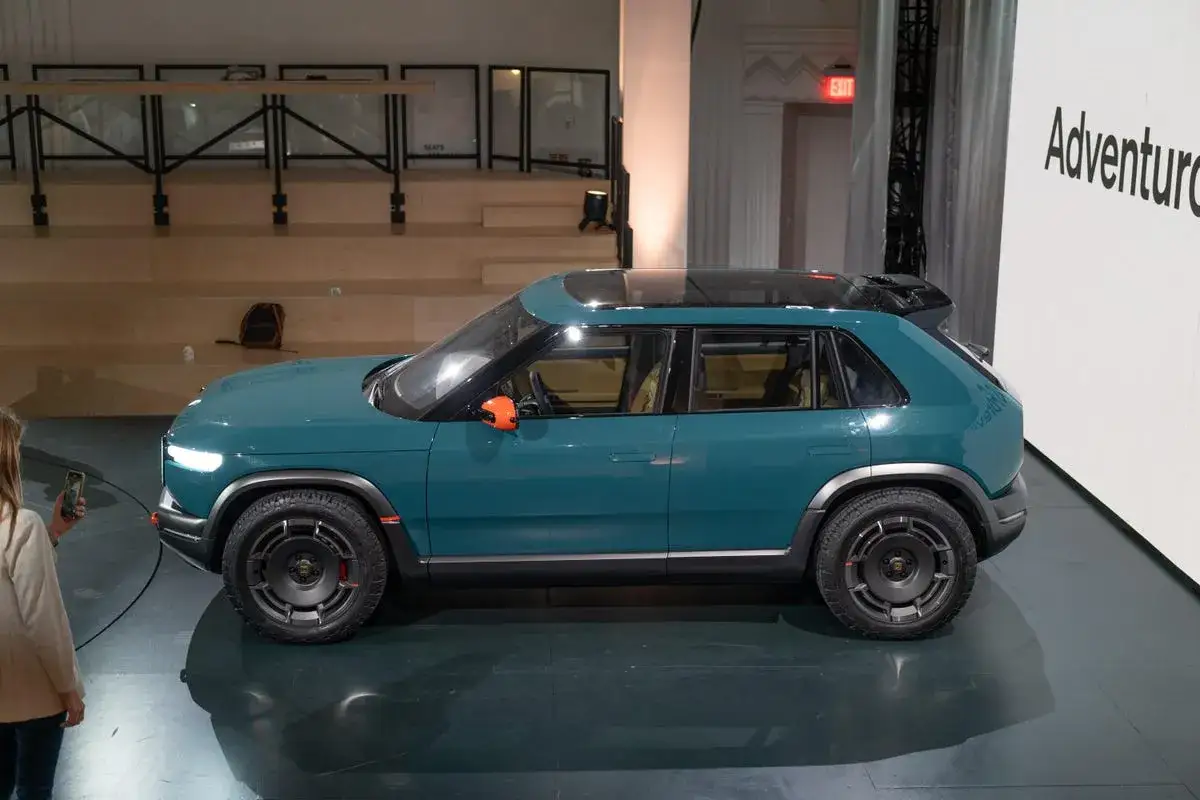 Rivian R3X, un SUV elettrico verde acqua con dettagli arancioni, pronto per l'avventura.