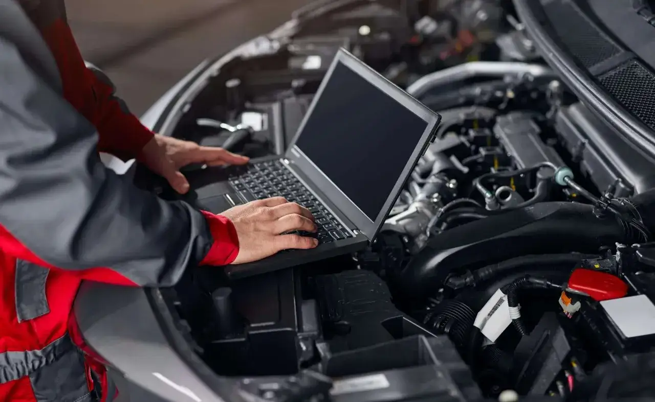 Meccanico con laptop esegue aggiornamento centralina auto, analizzando il motore per ottimizzare le prestazioni.
