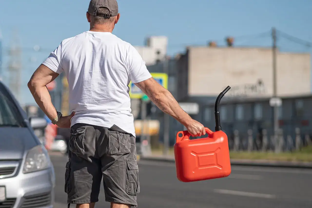Uomo con tanica rossa in mano, vicino a un'auto, con la benzina esaurita.