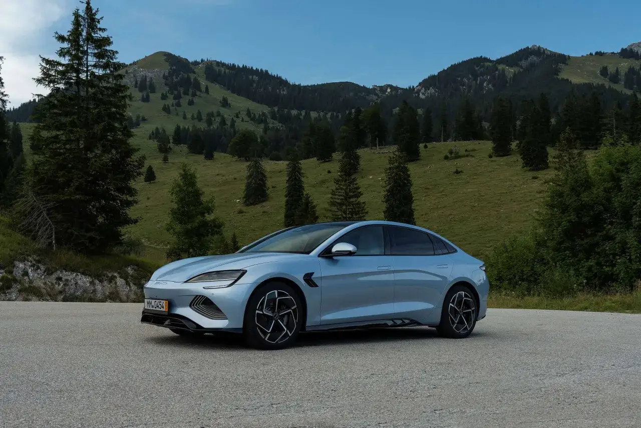 BYD Seal, un'auto elettrica con un'ottima autonomia, sfreccia su una strada alpina circondata da verdi colline e alberi.