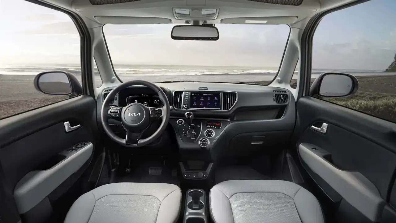 Interno della Kia Ray con vista sul mare. Volante, cruscotto moderno e sedili chiari.