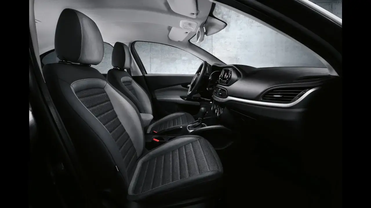 Interni della Fiat Egea: sedili bicolore in tessuto e pelle, cruscotto moderno e cambio manuale.